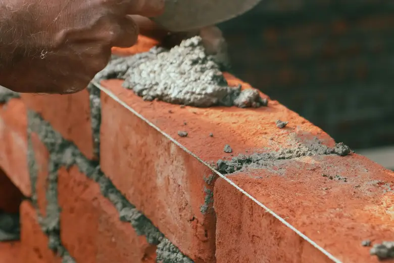 Hands laying a course of brick with a trowel